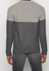 Stickad tröja med en tvåfärgad design, som har en ljusgrå övre del och en mörkgrå undre del. Texturerad tyg, rund halsringning.