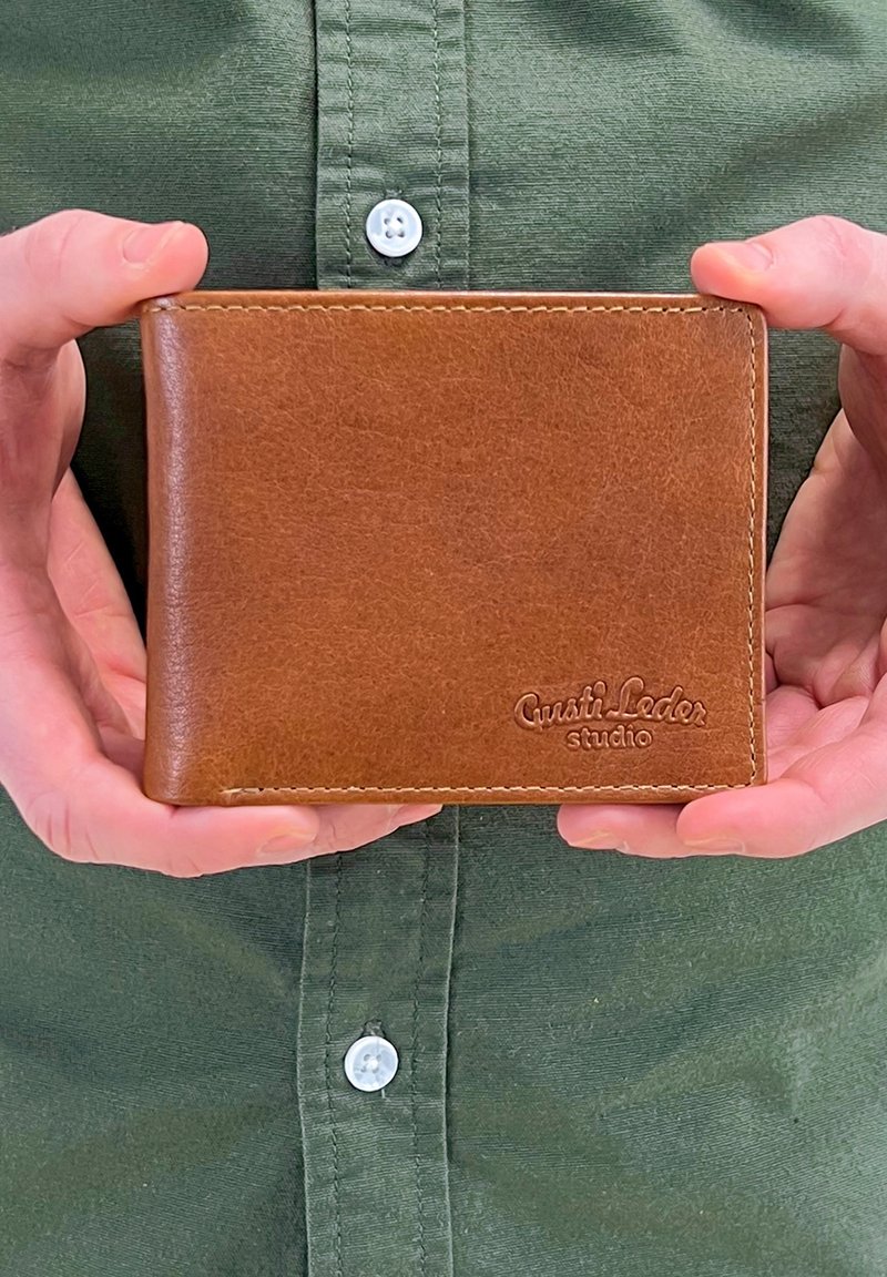 Brązowy skórzany portfel z teksturowaną powierzchnią, w formie bi-fold, z wytłoczonym logo, starannym szwem i eleganckim prostokątnym kształtem, trzymany między dwiema rękami.