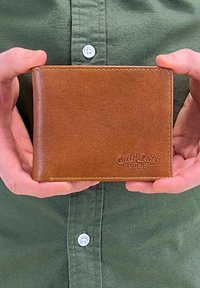 Brown leather wallet with a smooth texture and embossed branding. Features stitched edges and a rectangular design, held between hands.