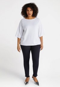 White, short-sleeve top with a round neckline and subtle dot pattern, paired with fitted dark jeans and silver pointy-toed shoes.