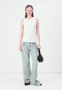 Hvit ribbet ermeløs topp, lyseblå vid benjeans, svart firkantet håndveske og sorte leiligheter. Modellen står mot en hvit bakgrunn.