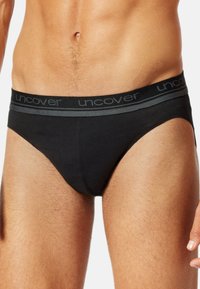 Culotte en coton noir avec une ceinture élastique grise portant le nom de la marque "uncover" dans un motif répété. Texture lisse et coupe ajustée.