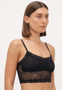Sort blonde bralette med blomsterbroderi, gennemsigtig mesh-stof, justerbare stropper og en scalloped blondekant langs kanterne.