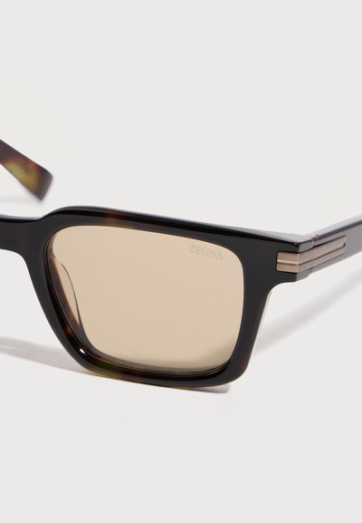 Ορθογώνια γυαλιά ηλίου με χρωματισμό χελώνας, φακούς με καφέ απόχρωση και διακριτικές μεταλλικές λεπτομέρειες στα πλαϊνά.