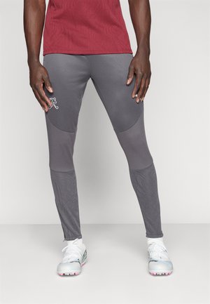 Graue Sportleggings aus strukturiertem Stoff, figurbetontem Design und Naht-Details. Mit einem Logo-Element am Oberschenkel. Kombiniert mit weißen Sportschuhen.