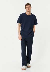 Marinblå bomull t-shirt med korta ärmar i en avslappnad passform, ihopparad med marinblå byxor. Skorna är vita med beigea detaljer.