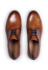 Bruine leren schoenen met een gladde afwerking, voorzien van marineblauwe veters, ronde neus en een witte rubberen zool. Eenvoudig ontwerp met minimale accenten.