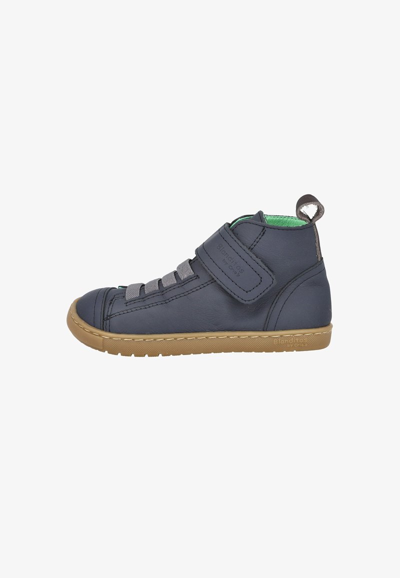 Zapato alto de cuero gris con correa de Velcro, suela de goma y un interior verde en contraste. Presenta cordones grises y una etiqueta de bucle en la parte trasera.