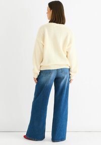 Crème gebreid sweater met een losse pasvorm en ribbels bij de manchetten, gecombineerd met hoge taille wijdlopende blauwe jeans met achterzakken.