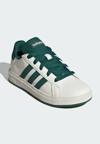 White sneaker with green accents, smooth leather upper, three green stripes on the side, and textured rubber sole. Green laces and logo.