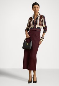 Μεταξωτή μπλούζα με αφηρημένο πολύχρωμο μοτίβο, μπορντό culottes με ψηλή μέση, μαύρη τσάντα χειρός με χρυσές λεπτομέρειες και μαύρα παπούτσια με ψηλό τακούνι.