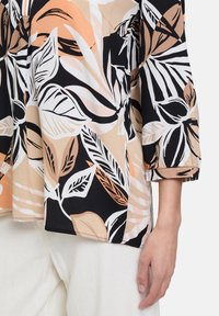 Lekka bluzka z mieszanką czarnych, białych i brzoskwiniowych wzorów liści, z rękawami o długości trzy czwarte i miękką teksturą materiału.