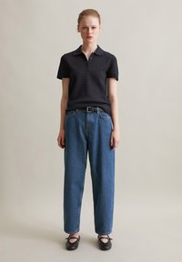 Zwart gestructureerd poloshirt met korte mouwen, gecombineerd met blauwe hooggesneden jeans met rechte pijpen en zwarte platte schoenen met strikken.