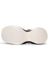 Podešev boty s texturovaným černým gumovým povrchem a kontrastním, světle krémovým, vzorovaným dnem. Obsahuje definované drážky pro trakci.