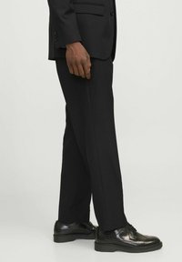 Czarne spodnie garniturowe o gładkiej fakturze, w kroju slim fit. Noszone z wypolerowanymi czarnymi butami akcesoryjnymi z detalami w stylu brogue.