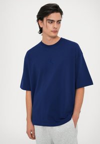 Námornícky modré oversized bavlnené tričko s okrúhlym výstrihom a vyšitým logom na hrudi, spárované s svetlošedými teplákmi.
