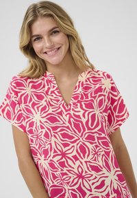 Tunic a maniche corte e scollo a V in rosa e crema, caratterizzata da un motivo floreale con contorni bold e una vestibilità comoda. Tessuto testurizzato.