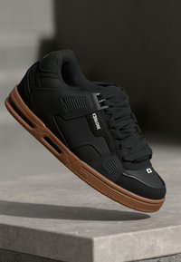 Sorte sneakers med en tekstureret overdel, polstret krave og brun gummisål. Har minimal branding og snørrelukning.