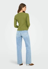 Groene geribbelde lange mouwen bovenstuk met een getailleerd ontwerp, gecombineerd met lichtblauwe rechte jeans en bruine hakken.