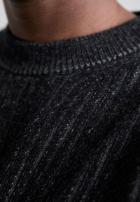 Pull en maille gris foncé présentant une texture côtelée et un col rond classique. Le tissu semble épais et chaud, avec une légère variation de couleur.