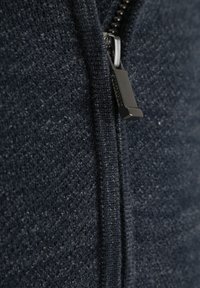 Marineblauwe jas met ritssluiting en een gestructureerde stof. Het ritsbeslag is metallic zilver en de stof heeft een diagonale patroon.