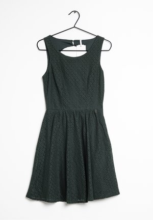 Dunkelgrünes, ärmelloses Kleid aus strukturiertem, gemustertem Stoff; enganliegendes Oberteil, das in einen ausgestellten Rock übergeht. Mit einem Rückenschlitz als Schlüsselöffnung.