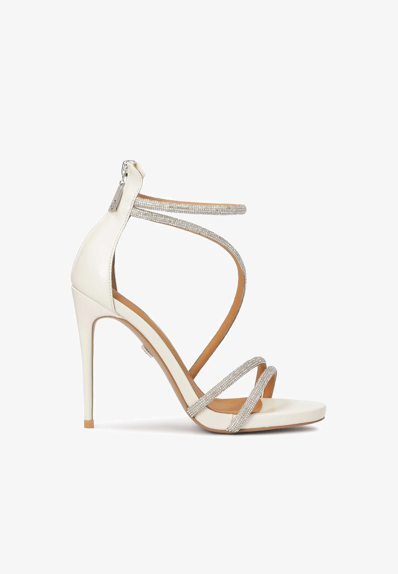 Baltas augstpapēžu sandaļi ar spīdīgām sudraba siksnām, atvērtu purngalu un rāvējslēdzēju aizmugurē. Gluda tekstūra, elegants dizains un smailais papēdis.
