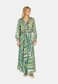 Abito maxi in verde, giallo e blu con un motivo ondulato. Presenta un colletto arricciato e maniche lunghe, realizzato in un tessuto leggero e trasparente.