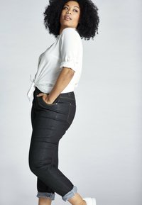 Tummansiniset farkut, joiden lahkeet on käännetty, kultaisilla ompeleilla ja sivutaskuilla, yhdistettynä valkoiseen paitaan, joka on sidottu vyötärölle.