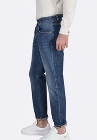 Jeans in denim blu scuro con una vestibilità comoda, caratterizzati da una gamba dritta, risvolti arrotolati e un leggero effetto slavato. Abbinati a sneakers bianche.