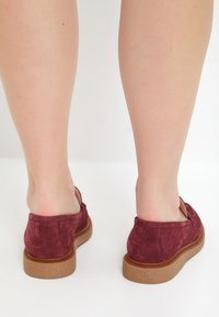 Bordeaux farvede slip-on sko lavet af blødt ruskind med en komfortabel struktureret sål. Åben bagside design med subtile stikninger.