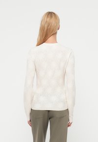 Λευ κό τοπ με μακριά μανίκια και floral σχέδιο, ημιδιαφανής υφή, στρογγυλεμένος λαιμός και εφαρμοστή γραμμή. Πλάγια όψη πίσω με ομαλή υφή υφάσματος.