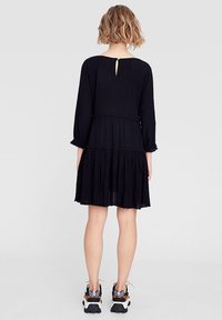 Svart klänning med långa ärmar, lagerdesign och volangdetaljer. På baksidan finns en liten nyckelhålsöppning. Bärs med klumpiga sneakers.