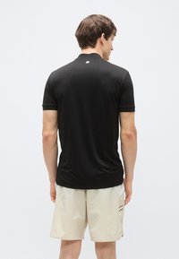 Svart polo t-skjorte med korte ermer, med en subtil logodetalj på baksiden og en glatt tekstur, kombinert med lys beige shorts.