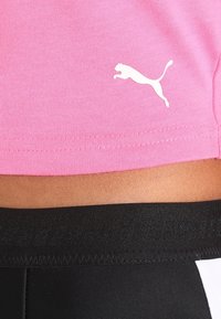 Rosa idrottströja med korta ärmar som har en vit Puma-logotyp; svart midjeband på matchande byxor med texturerad detalj.