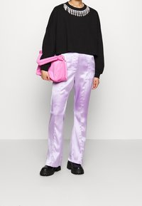 Felpa nera a maniche lunghe con collo decorato da perline, abbinata a pantaloni in satin lavanda e una borsa a tracolla rosa. Stivali neri con tacco basso.