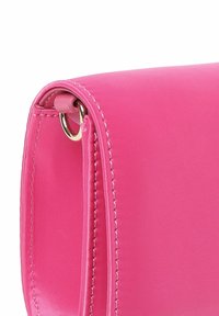 Borsa a mano rosa con una finitura liscia e testurizzata, caratterizzata da un dettagli in anello metallico dorato e cuciture a contrasto lungo i bordi.