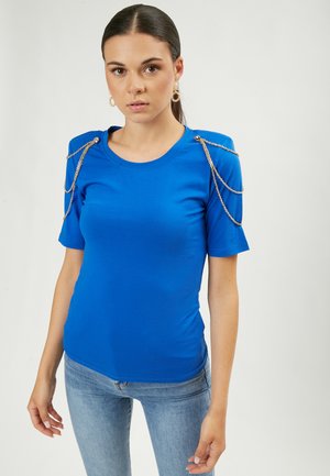 Camiseta azul ajustada de manga corta, con acentos decorativos de cadena dorada en los hombros. Tejido suave y cuello redondo clásico.