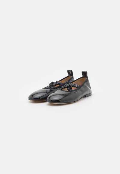 Zwarte gepatineerde leren balletschoenen met een ronde neus, voorzien van een gebogen zwarte strikaccent en een kleine hak. Gladde oppervlakte en elastische details.