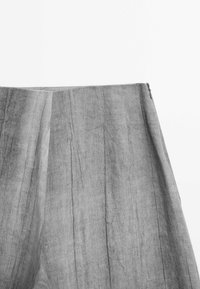 Pantalon en lin gris avec une finition texturée, doté de plis et d'une fermeture éclair, présentant un design moderne et épuré.