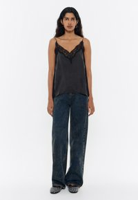 Camisola de satén negra con encaje en el escote, combinada con unos vaqueros de tiro alto, sueltos y desgastados en azul, y bailarinas negras con estampado.