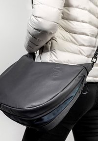 Borsa a tracolla in pelle nera con finitura testurizzata, zip visibile e tracolla regolabile. Caratterizzata da una fodera interna blu.