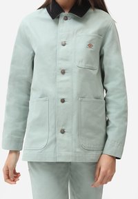 Jasnozielona bawełniana kurtka z czarnym kołnierzem z sztruksu, zapinana na guziki, z dwoma przednimi kieszeniami. Na kieszeni na piersi znajduje się małe logo.