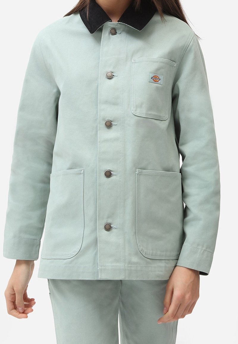 Jasnozielona bawełniana kurtka z czarnym kołnierzem z sztruksu, zapinana na guziki, z dwoma przednimi kieszeniami. Na kieszeni na piersi znajduje się małe logo.