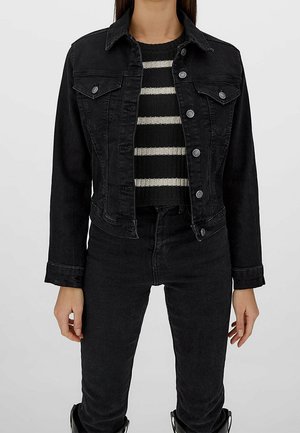 Schwarze Jeansjacke mit Kragen, Fronttaschen und silbernen Knopfdetails, kombiniert mit einem gestreiften schwarzen und metallischen Pullover.