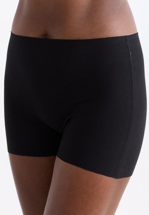 Close-up of a person wearing smooth black fitted shorts with a high waist and mid-thigh length against a plain background.