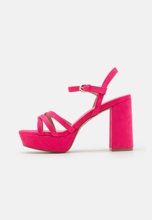 Bright pink suede high-heeled sandal with thick block heel, platform sole, three front straps, and adjustable ankle strap with gold buckle.