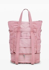 Mochila de lona rosa con asas resistentes, múltiples bolsillos exteriores, cierre de cremallera y acabado texturizado. La base cuenta con un compartimento con cremallera.
