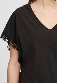 Zwarte V-hals top met korte mouwen en delicate kantafwerking. De stof heeft een licht gestructureerde uitstraling, wat zorgt voor een casual uitstraling.
