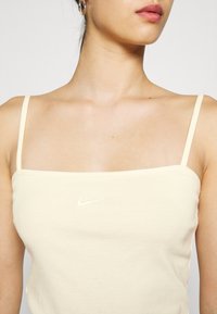 Beige linne med tunna remmar, gjort av mjukt tyg. Har en liten vit Nike-logga på framsidan. Enkel, figurnära design.